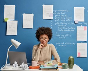 Jeune femme à son bureau avec des feuilles collées derrière elle