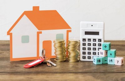 Maquette de maison avec à côté une calculatrice des clefs et des pièces de monnaie