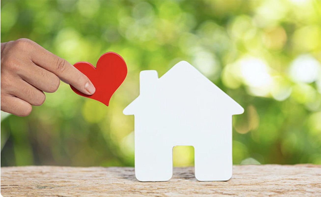 Main tenant un coeur en papier près d'une maison blanche en papier