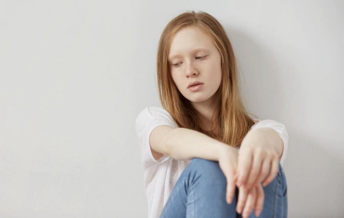 Jeune femme triste assise contre un mur
